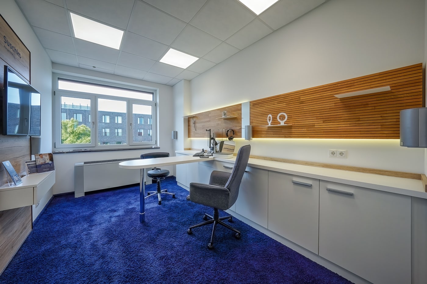 Ein Beratungsraum mit moderner Einrichtung und blauem Teppich in einem Hörgeräte-Fachgeschäft